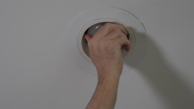 Electrician installing new light bulb in recessed ceiling light fixture. Man replacing burned out incandescent light bulb.