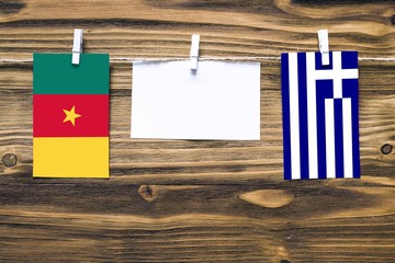 Hanging flags of Cameroon and Greece attached to rope with clothes pins with copy space on white note paper on wooden background.Diplomatic relations between countries.