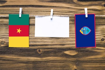 Hanging flags of Cameroon and Guam attached to rope with clothes pins with copy space on white note paper on wooden background.Diplomatic relations between countries.