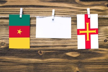 Hanging flags of Cameroon and Guernsey attached to rope with clothes pins with copy space on white note paper on wooden background.Diplomatic relations between countries.