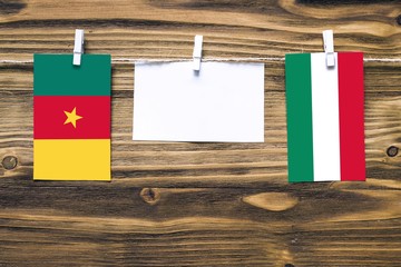 Hanging flags of Cameroon and Hungary attached to rope with clothes pins with copy space on white note paper on wooden background.Diplomatic relations between countries.