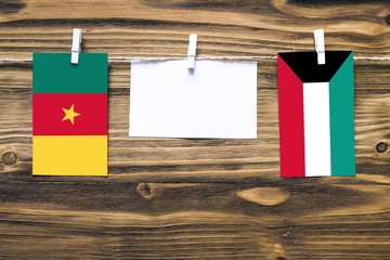 Hanging flags of Cameroon and Kuwait attached to rope with clothes pins with copy space on white note paper on wooden background.Diplomatic relations between countries.