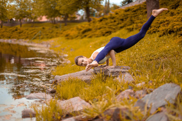 A young sports girl practices yoga on a fall yellow lawn by the river, use yoga assans posture. Meditation and unity with nature
