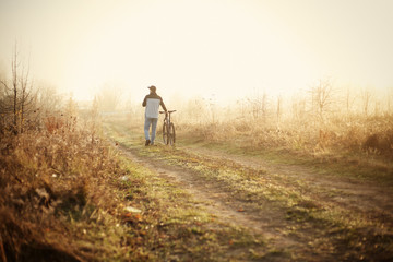 A man walks with a bicycle in morning fog.