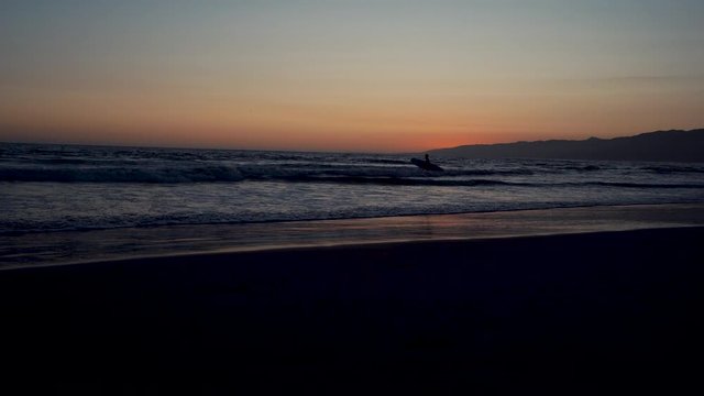 Sunset on the Pacific Coast in California, surfer and joggers run a sport