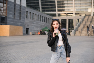 Portrait of european young beautiful smiling woman with dark straight hair in black leather jacket and blue jeans on city background