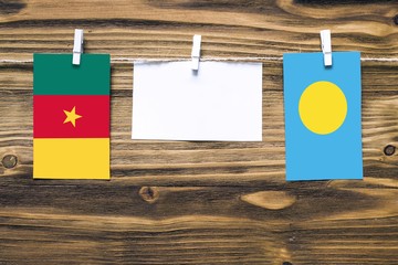 Hanging flags of Cameroon and Palau attached to rope with clothes pins with copy space on white note paper on wooden background.Diplomatic relations between countries.