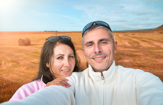 Happy couple taking a selfie in open countryside with hay bales on the background