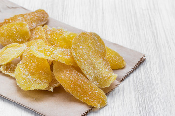 Oval slices of dried ginger in sugar lie on a paper bag on a white wooden background, side view from above