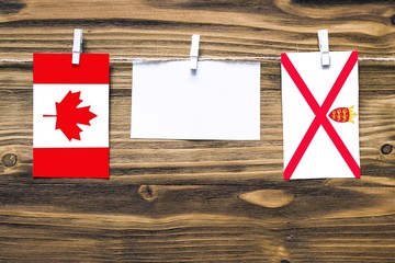 Hanging flags of Canada and Jersey attached to rope with clothes pins with copy space on white note paper on wooden background.Diplomatic relations between countries.