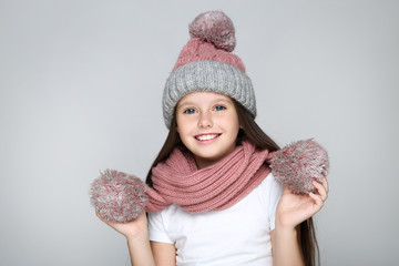 Little girl in hat and scarf on grey background