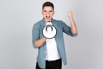 Young man screaming in megaphone on grey background