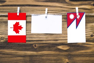 Hanging flags of Canada and Nepal attached to rope with clothes pins with copy space on white note paper on wooden background.Diplomatic relations between countries.