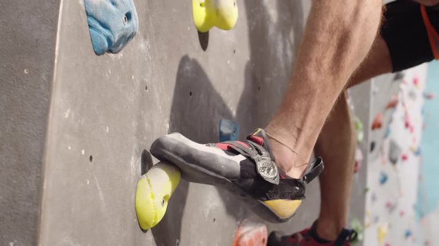 Close up of legs of sportsman wearing special sneakers climbing artificial boulder in indoor climbing center
