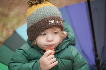 little child eat cookie with a colored rainbow umbrella in the Park. 2 year old baby in autumn