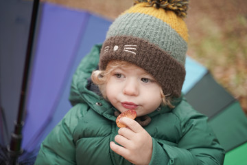 little child eat cookie with a colored rainbow umbrella in the Park. 2 year old baby in autumn