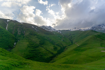 Naklejka premium Landscape mountain view peaks in snow and green hills, deep blue sky and huge white clouds background, Caucasian mountains, Kazbek mountain
