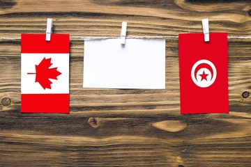 Hanging flags of Canada and Tunisia attached to rope with clothes pins with copy space on white note paper on wooden background.Diplomatic relations between countries.