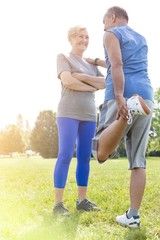 Fototapeta premium Senior man performing quad stretch while taking support of woman in park