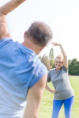 Senior woman doing side bend exercise with man in park