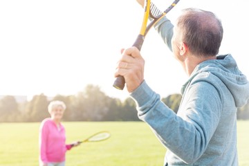 Senior man serving badminton in park on sunny day