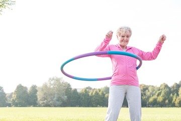 Senior woman doing gymnastic with hula hoop in park © MDBPIXS