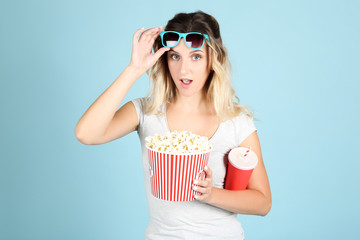 Obraz premium Young woman holding bucket with popcorn and paper cup on blue background