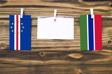 Hanging flags of Cape Verde and Gambia attached to rope with clothes pins with copy space on white note paper on wooden background.Diplomatic relations between countries.