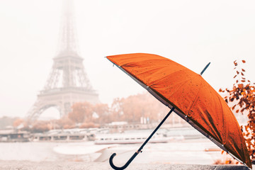 Bright orange umbrella on a rainy autumn foggy day in Paris against the background of the Eiffel tower