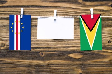Hanging flags of Cape Verde and Guyana attached to rope with clothes pins with copy space on white note paper on wooden background.Diplomatic relations between countries.