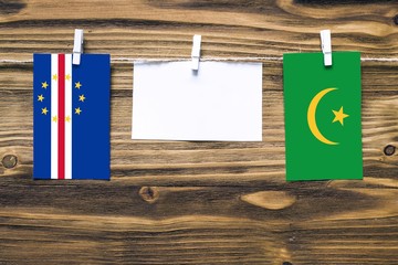 Hanging flags of Cape Verde and Mauritania attached to rope with clothes pins with copy space on white note paper on wooden background.Diplomatic relations between countries.