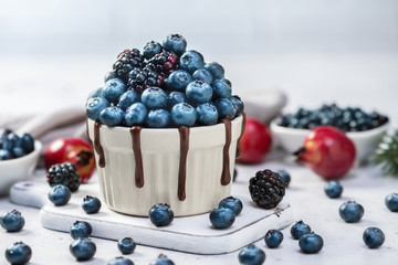 Chocolate mug cake with blueberries and blackberries in a white ceramic mug on white background