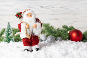 Christmas decor with Santa Claus toy, fir tree branches, sparkling balls and snow.