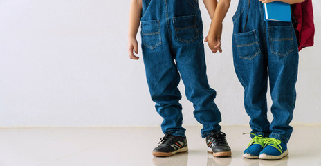 Leg of brother and sister wear blue jeans standing together on white background. Back to school concept.