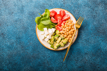 Obraz na płótnie Canvas Buddha Bowl with Avocado, chickpea, feta cheese, fresh spinach, Tomatoes and glass of water. Concept for healthy vegetarian detox balanced meal. Top view. Copy space.