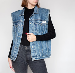 Young woman wearing stylish outfit with an oversized denim vest, black turtleneck and black jeans isolated on light grey background. Copy space