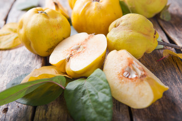 Ripe large quince fruit and slice   with green foliage in late autumn on brown wooden table. top view