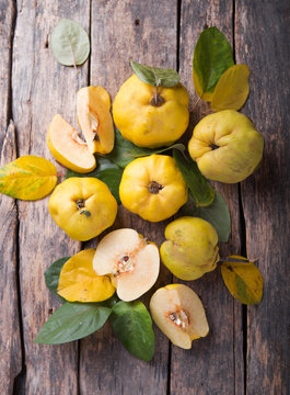 Ripe large quince fruit and slice   with green foliage in late autumn on brown wooden table. top view