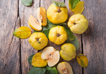 Naklejka na ściany i meble Ripe large organic quince fruit and slice with green foliage in late autumn on brown wooden table. top view