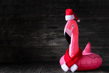 Inflatable pink flamingo in Santa Claus hat and red scarf on wooden rustic background