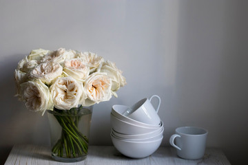 bouquet of white roses in a glass vase and pumpkins in a bowl on a white table as a decoration of the kitchen interior