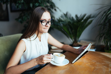 a student with a tablet pc is going to take a sip of coffee at a cafe table with pleasure