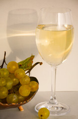  Bunches of white grapes in a vase and a glass of white wine on a light background with their reflection