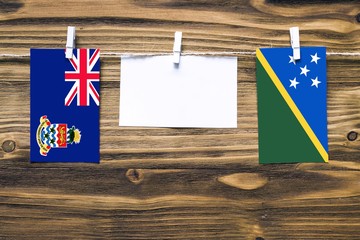 Hanging flags of Cayman Islands and Solomon Islands attached to rope with clothes pins with copy space on white note paper on wooden background.Diplomatic relations between countries.