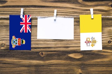 Hanging flags of Cayman Islands and Vatican City attached to rope with clothes pins with copy space on white note paper on wooden background.Diplomatic relations between countries.