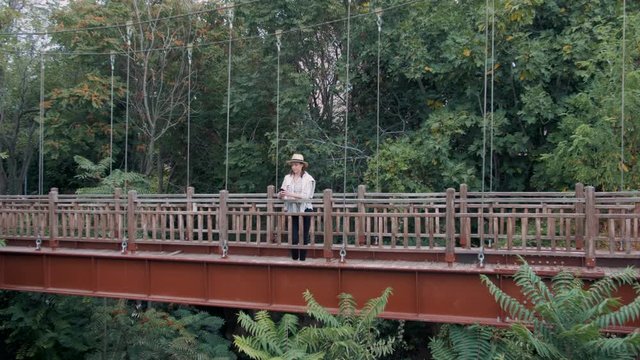 Millennial hipster woman tourist using smartphone on the bridge in the jungle.