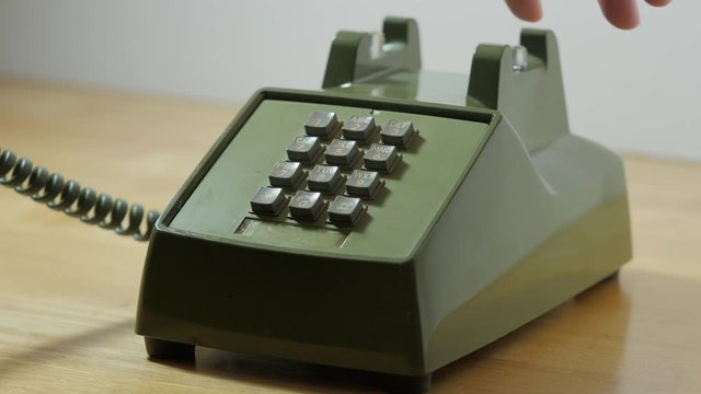 Man checking dial tone on retro push button rotary dial telephone. Making phone call on vintage avocado green landline phone.