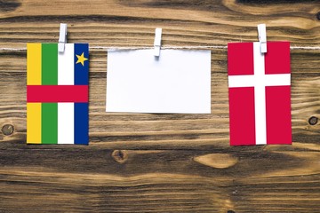 Hanging flags of Central African Republic and Denmark attached to rope with clothes pins with copy space on white note paper on wooden background.Diplomatic relations.