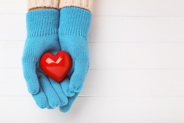 Hands in knitted mittens holding heart on white wooden table