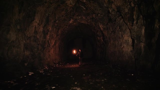 Man lost and afraid inside a natural cave illuminated by a flame torch. 4k